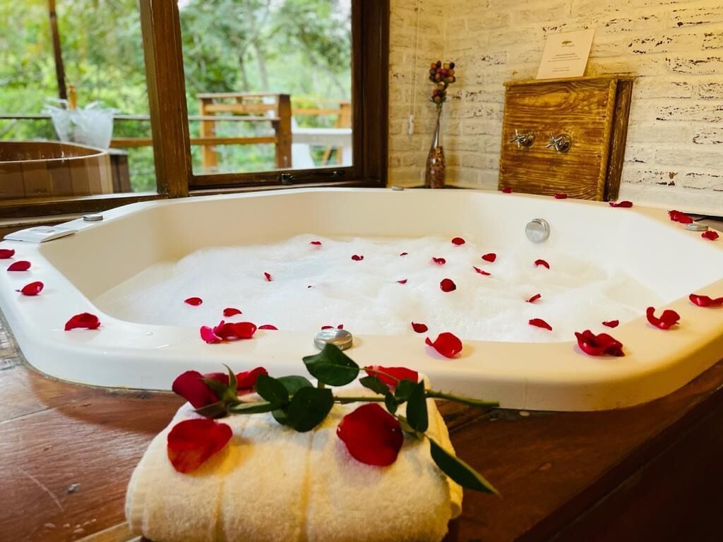 Eine mit Wasser und Rosenblättern gefüllte Badewanne, mit einem Handtuch und einer Blumenvase daneben.