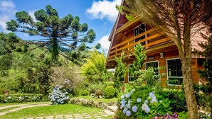 A wooden cabin with a garden in front, surrounded by trees and greenery. - Pousada Solar d'Araucária (Gonçalves)