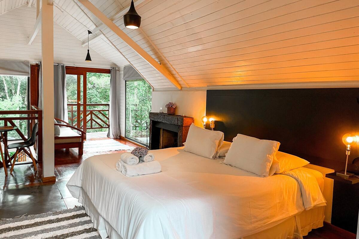Une chambre spacieuse avec un grand lit, une cheminée et un balcon agrémenté de meubles en bois.