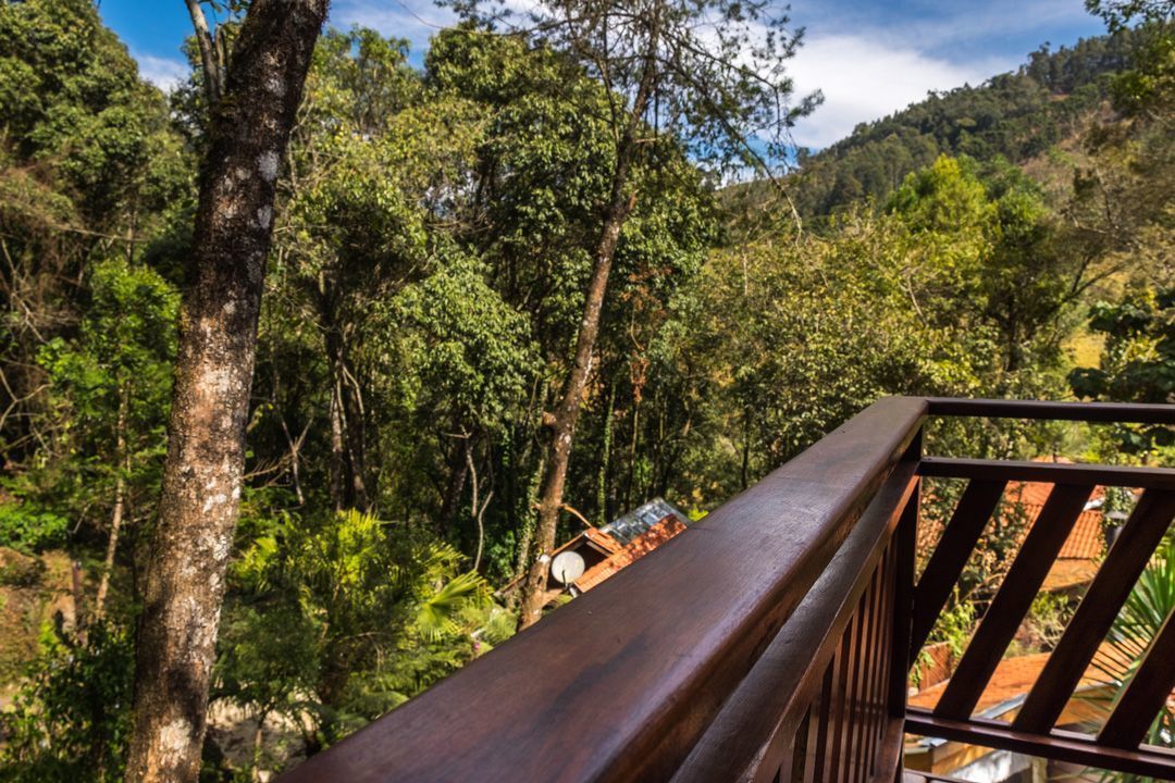 Grade de madeira varanda com vista para uma área verde e florestada, com uma casa ao fundo.