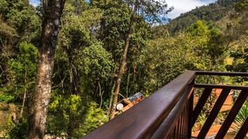 Grade de madeira varanda com vista para uma área verde e florestada, com uma casa ao fundo.