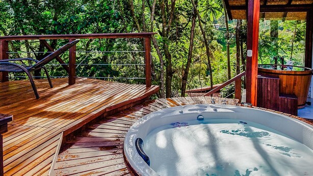 A wooden deck with a hot tub, surrounded by lush greenery. - Pousada Solar d'Araucária (Gonçalves)