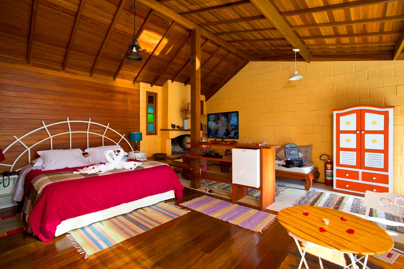 A cozy room with a bed, a small table, a television, and a fireplace.