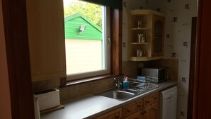 A kitchen with wooden cabinets, a window, a microwave, and a dishwasher. - Inverness Apartments - Culduthel (Inverness)