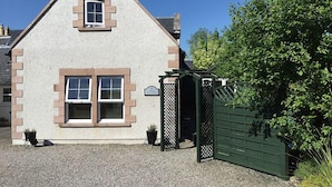 A house with a triangular roof, a small front porch, and a green gate. - Inverness Apartments - New Cottage (Inverness)