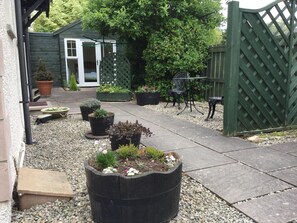 Un jardín con plantas en macetas, un banco de madera y una mesa de metal.