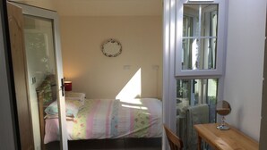 A bedroom with a bed, a wooden chair, a small table with a mirror, and a window. - Inverness Apartments - New Cottage (Inverness)