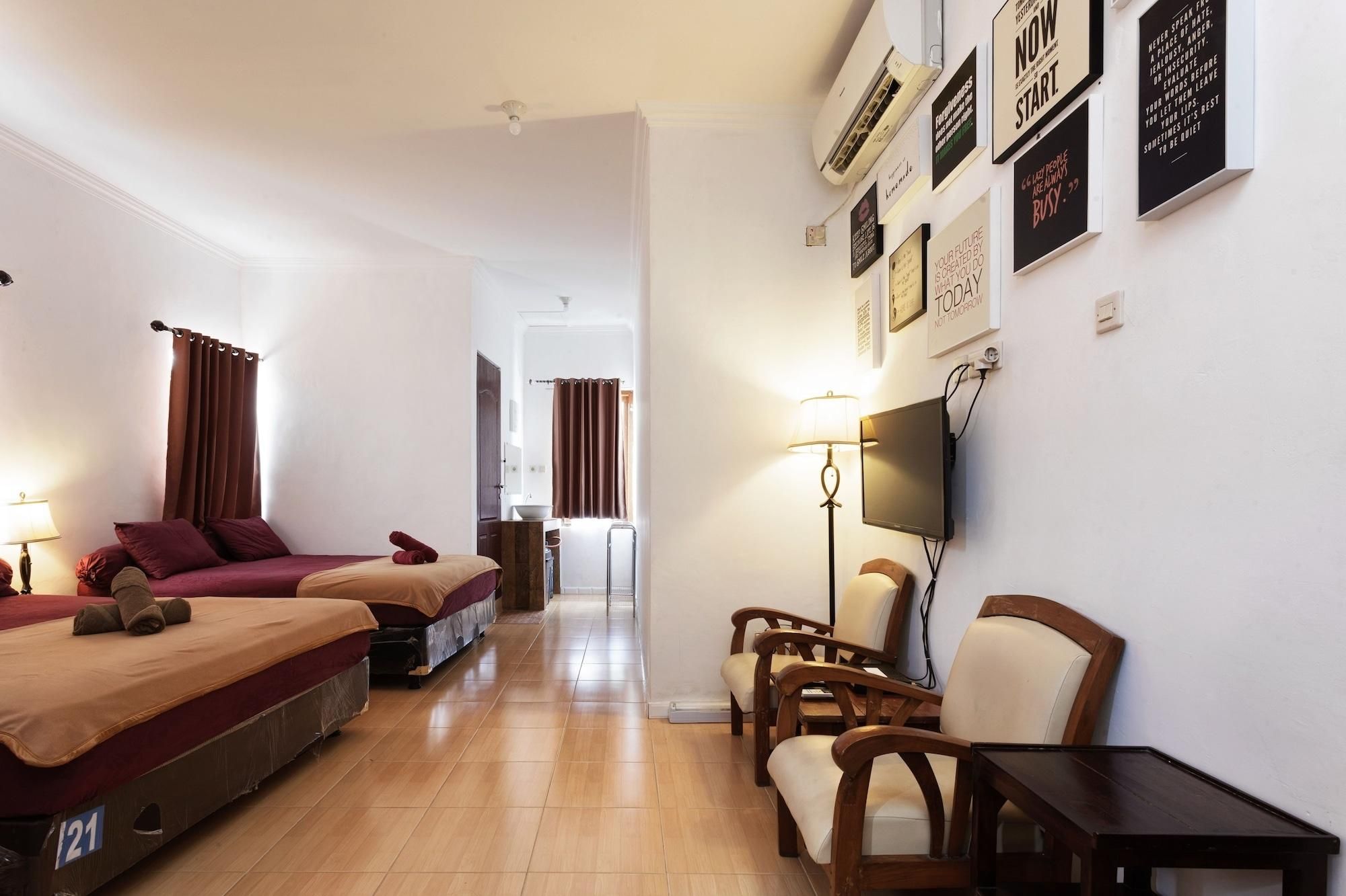Habitación de hotel con dos camas, un escritorio, un televisor y una pared con carteles motivacionales.