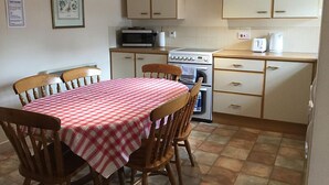 A compact kitchen with a dining table covered by a checkered tablecloth, wooden chairs, a microwave, an oven, and cabinets.