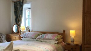 A bedroom with a bed, two bedside tables, a mirror, a lamp, and a window with curtains.