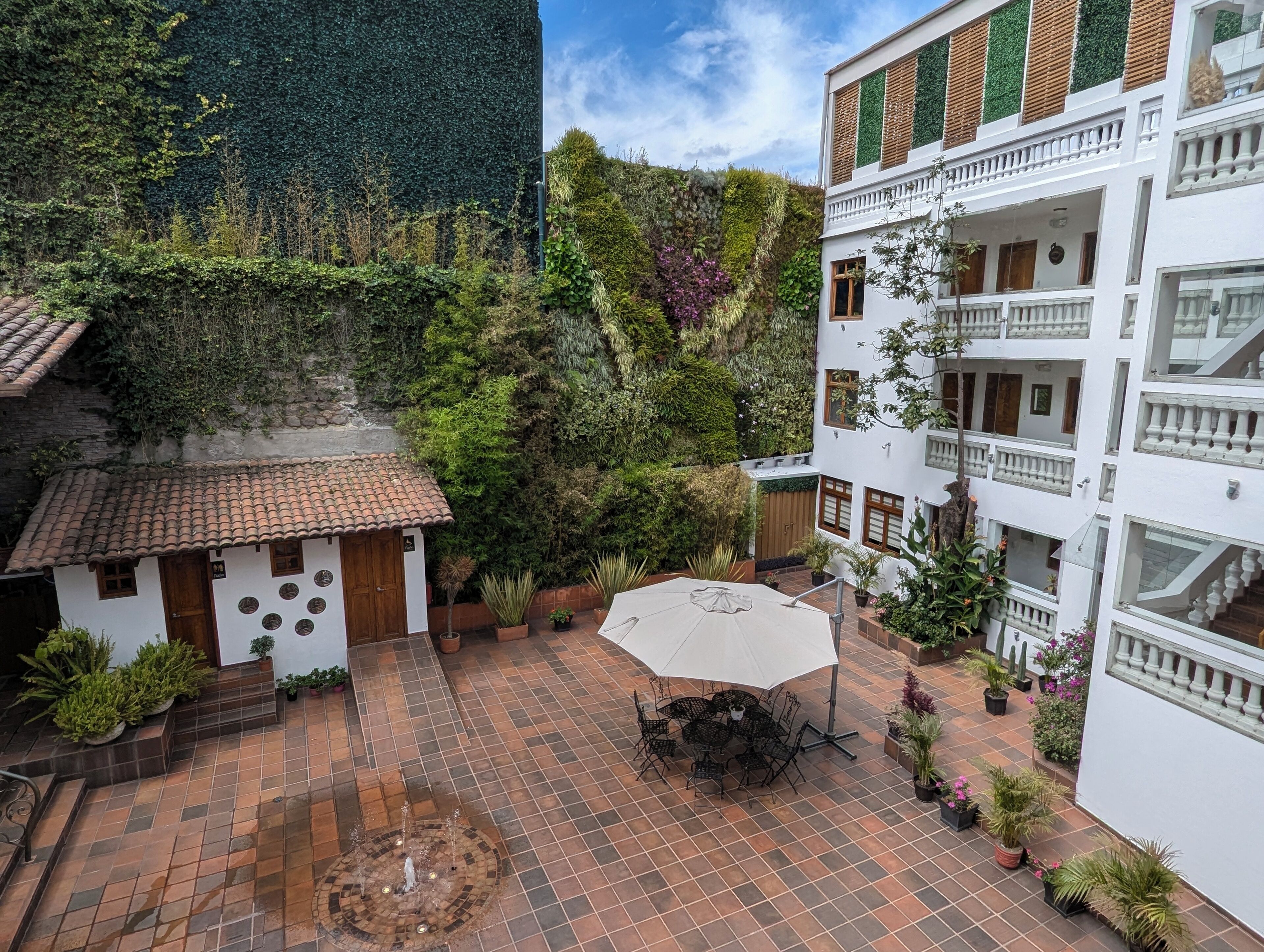 A courtyard with a tiled patio, a small building with a tiled roof, and a white building with balconies.