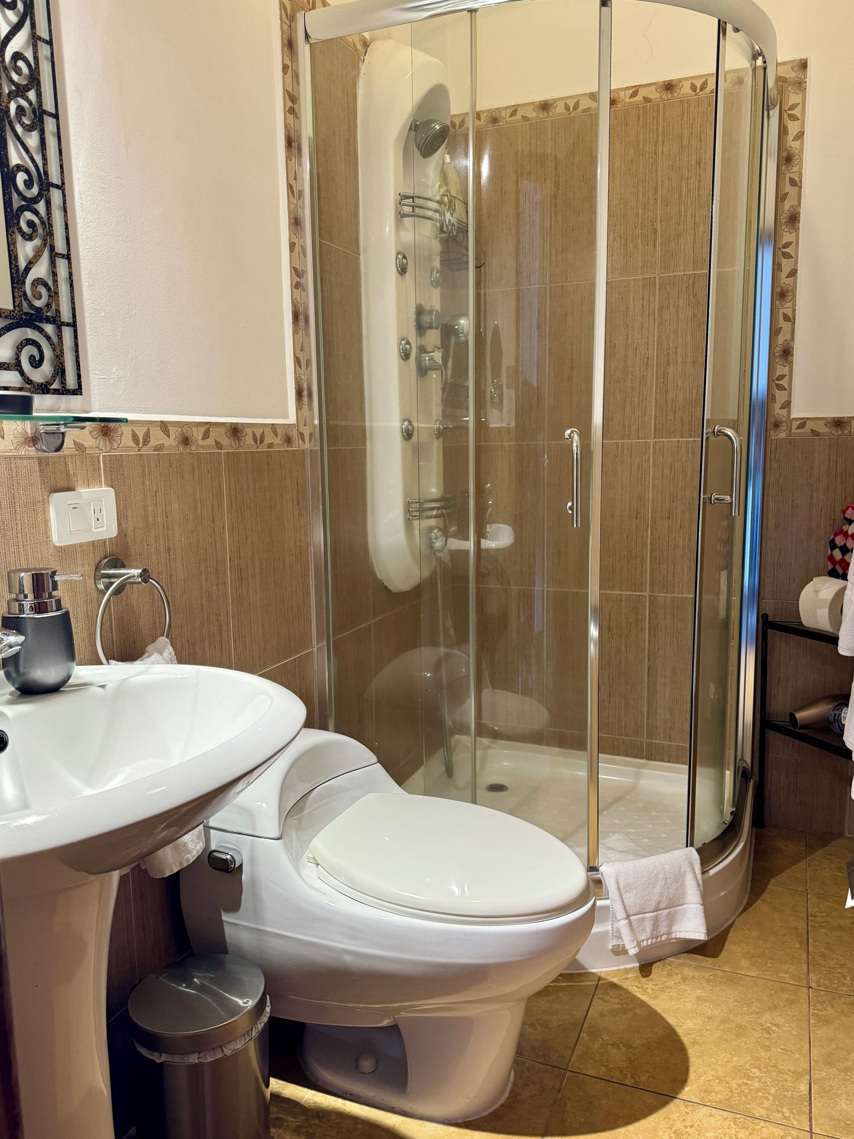 Un baño con ducha de vidrio, lavamanos, inodoro y un cubo de basura.