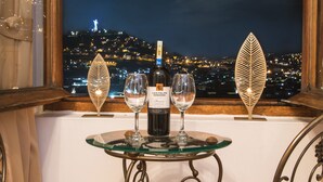 Taula amb ampolla i dues copes, dues cadires de vimet i vista d'un paisatge urbà de nit.