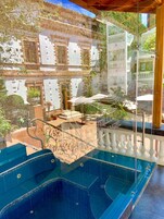 En swimmingpool med glasgelænder, en terrasse med udendørs møbler og udsigt til en historisk bygning.