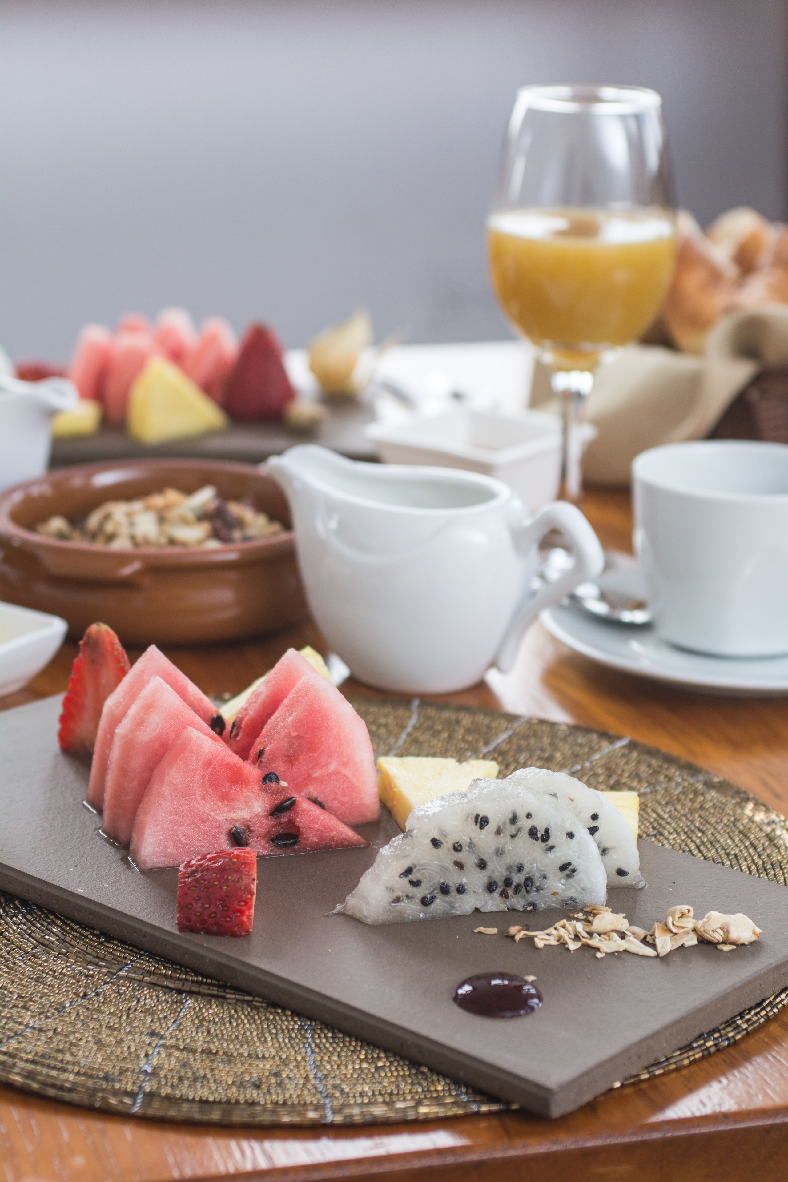 Desayuno con frutas variadas y un vaso de zumo de naranja sobre una mesa de madera.
