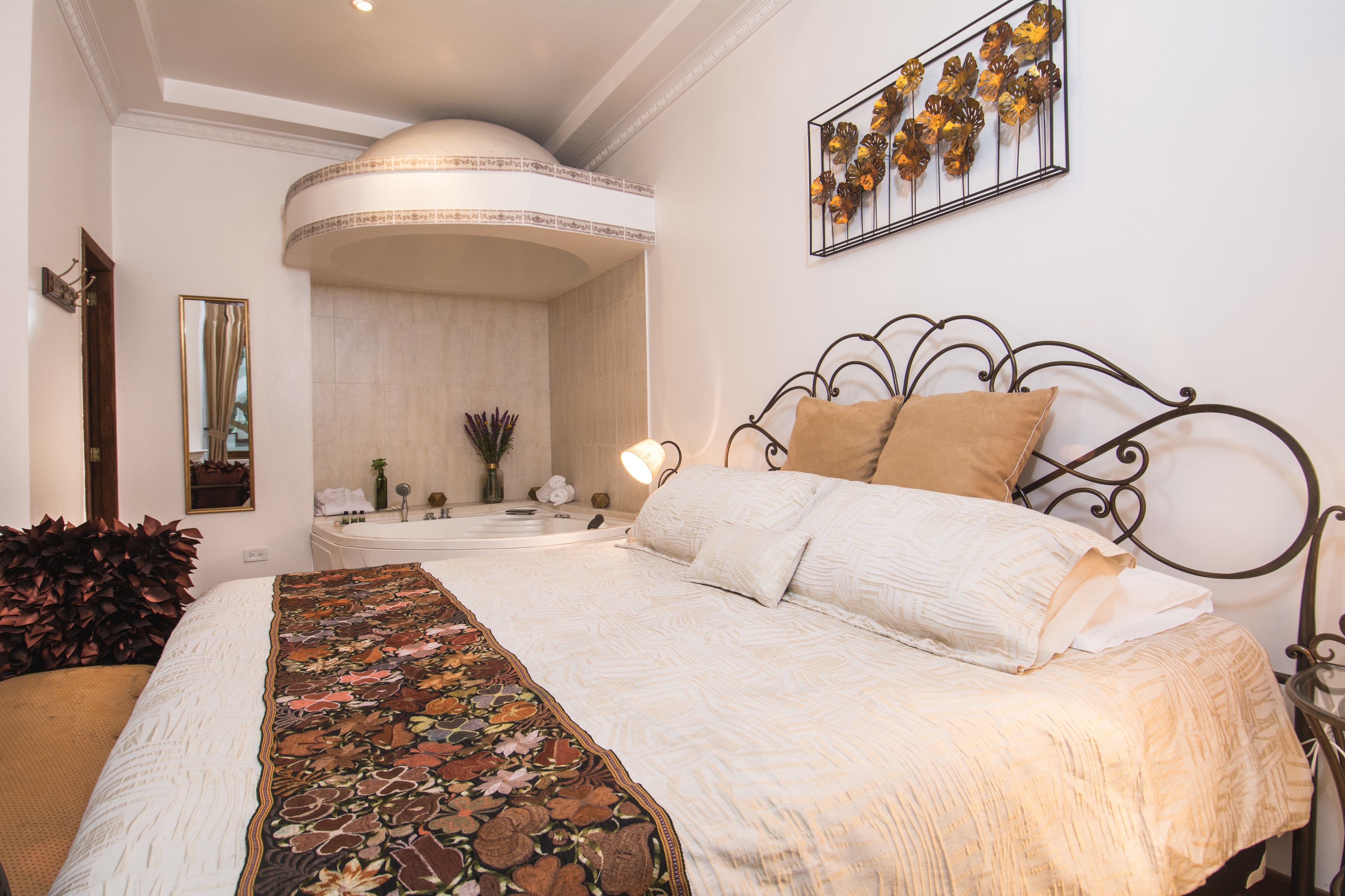 A bedroom with a large bed, a curved ceiling, a wall-mounted artwork, and a nightstand with a lamp.