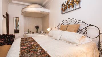 A bedroom with a large bed, a curved ceiling, a wall-mounted artwork, and a nightstand with a lamp.