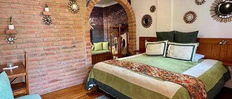 Un dormitorio con pared de ladrillo, cama de madera, colcha verde y espejos decorativos en la pared.