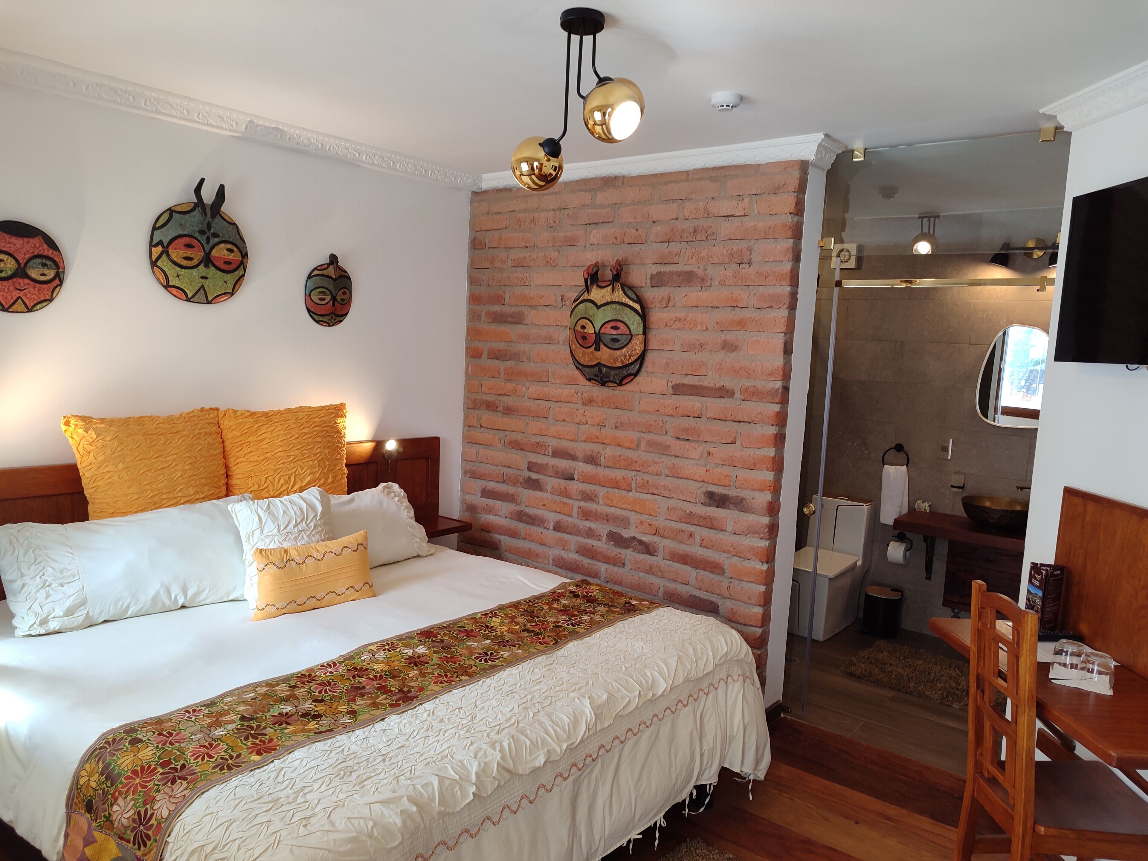 A bedroom with a brick wall, a bed with yellow and white pillows, a wooden headboard, and a decorative blanket.