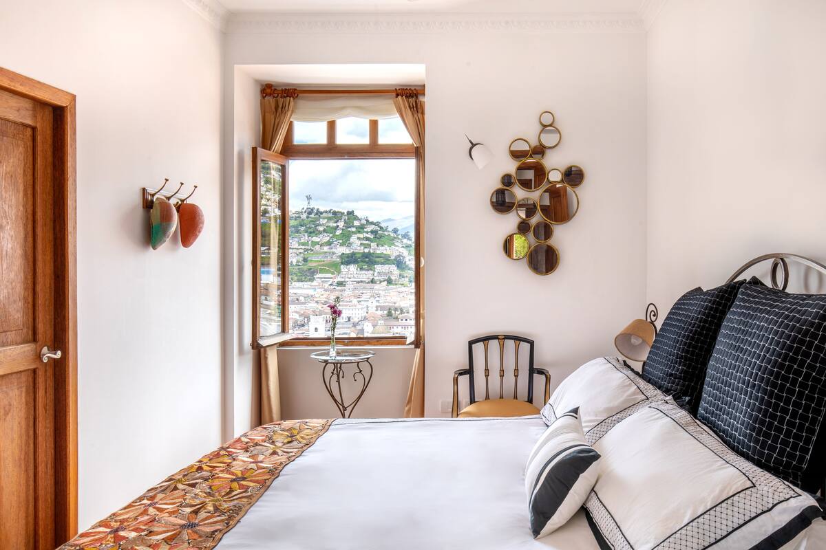 Een hotelkamer met een bed, een stoel, een klein tafeltje en een raam met uitzicht op een stadsbeeld.