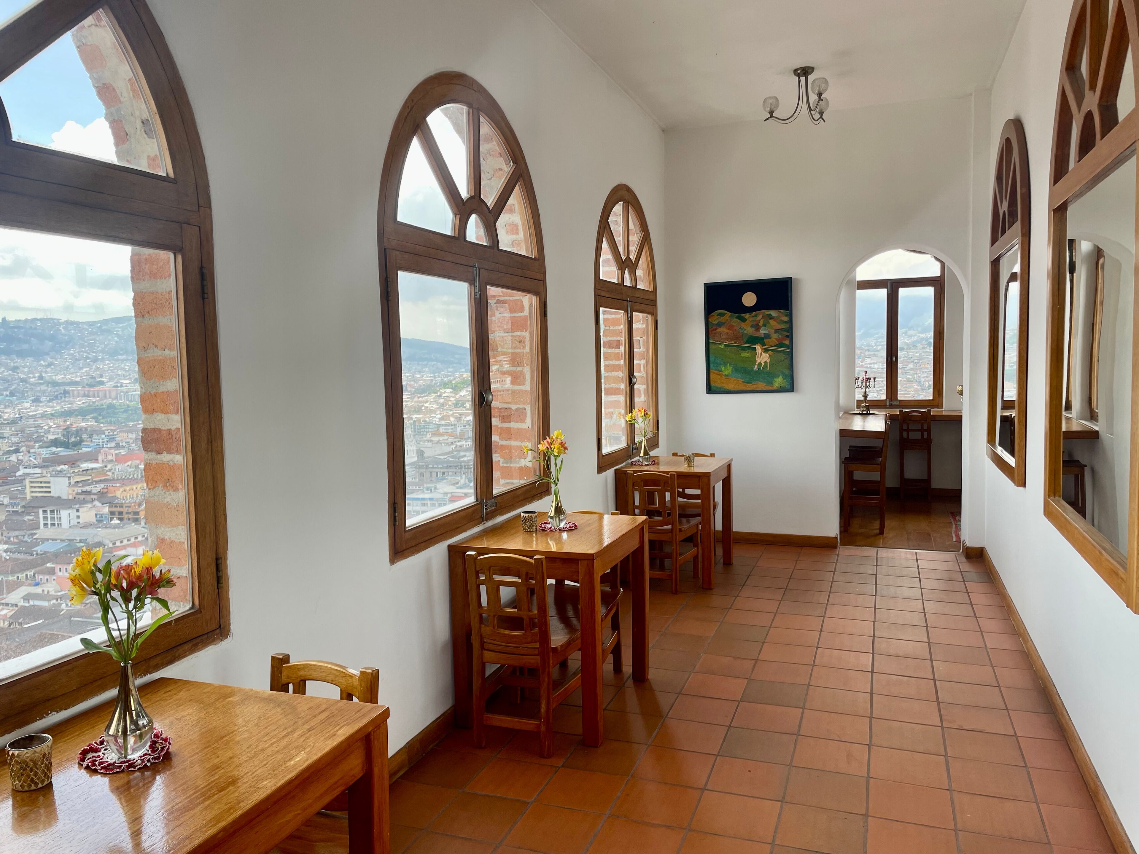 A dining area with high arched windows, a dining table, chairs, and a vase of flowers.