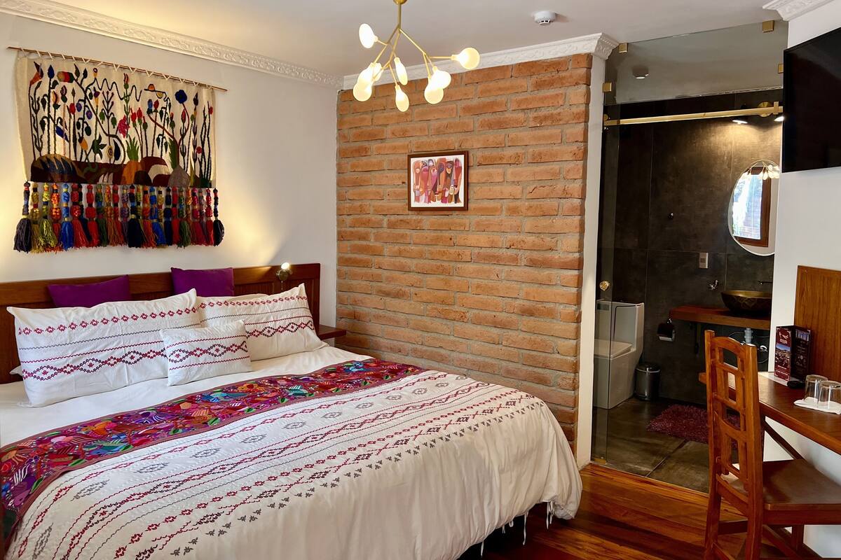 Een slaapkamer met een bakstenen muur, een bed met beddengoed met dessin, een hangende wandtapijt en een moderne kroonluchter.