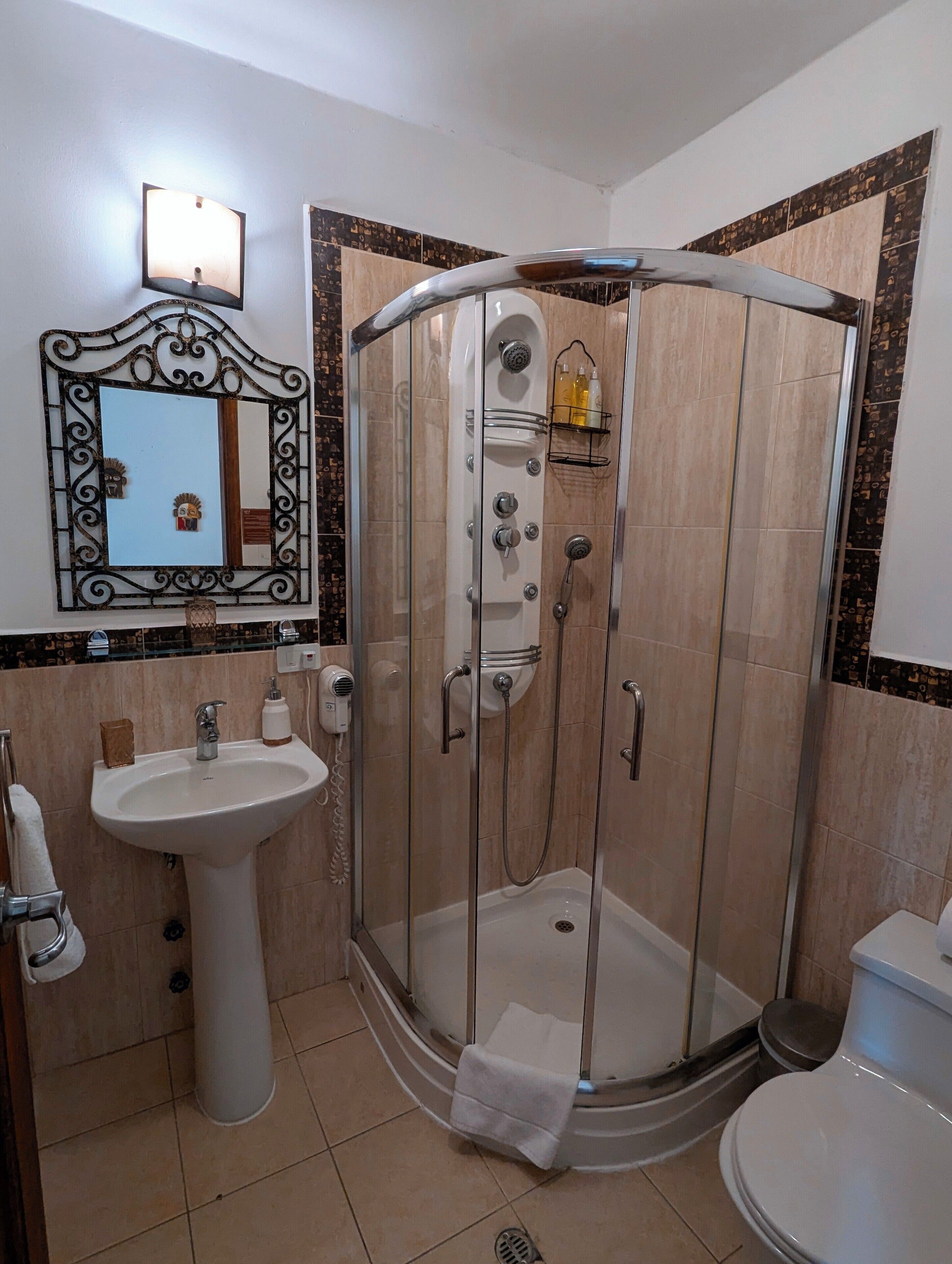A bathroom with a glass-enclosed shower, a pedestal sink, a toilet, and a mirror with a decorative frame.
