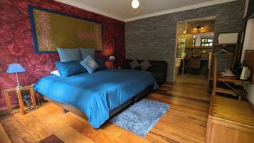 A bedroom with a bed, a wooden floor, a red accent wall, and a mirror.