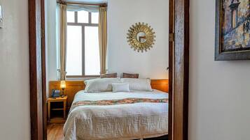 Un dormitorio con cama, mesita de noche, lámpara, espejo y un cuadro en la pared.