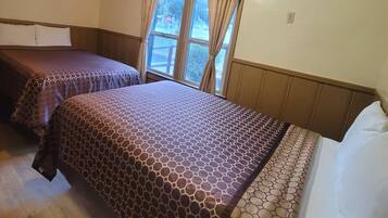 A hotel room with two beds, a window with curtains, an air conditioning unit, and a ceiling light.