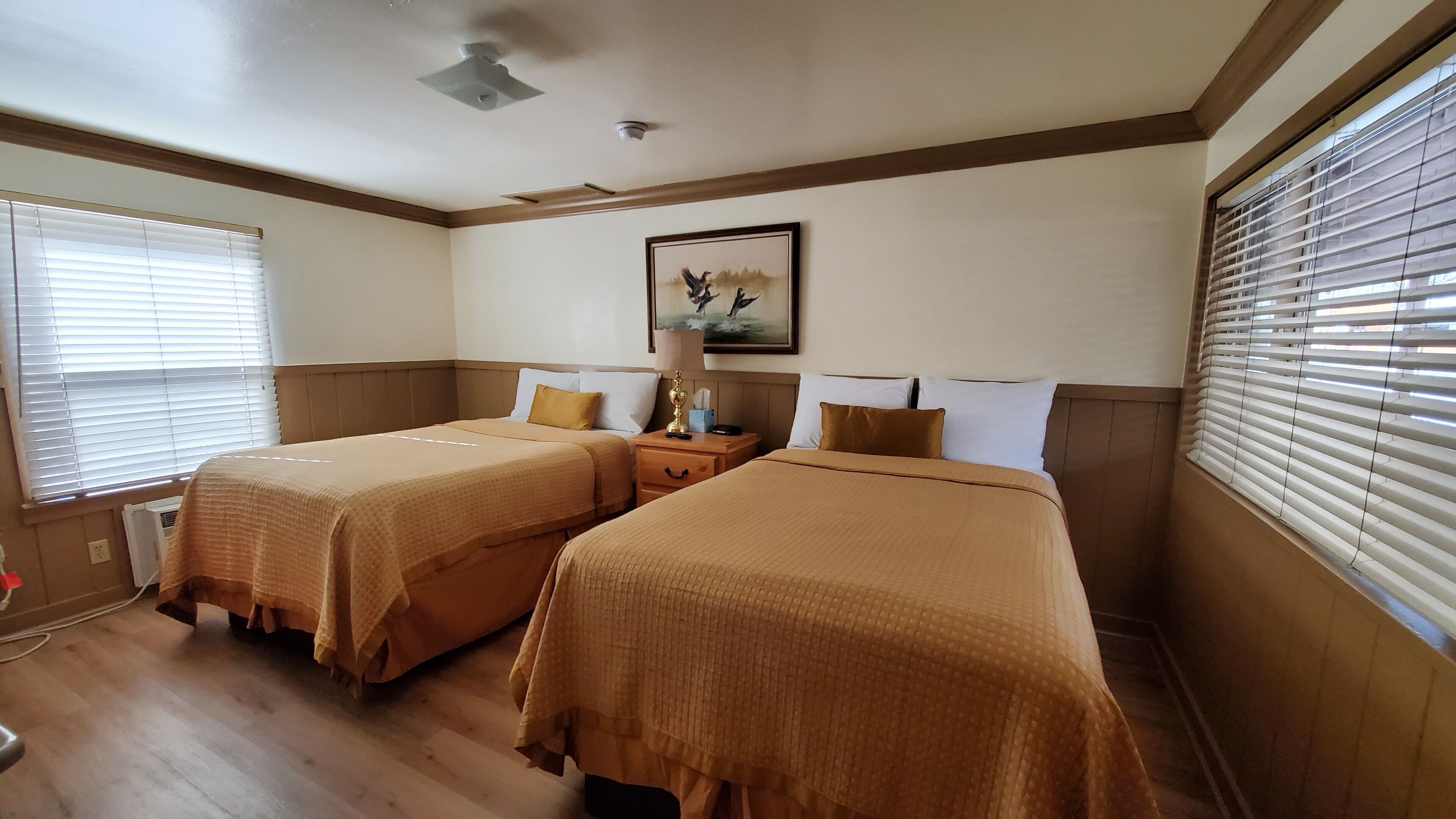A hotel room with two beds, a painting on the wall, and a window with blinds.