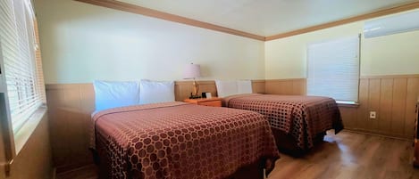 Habitación de hotel con dos camas, piso de madera, ventilador de techo y ventana con persianas.