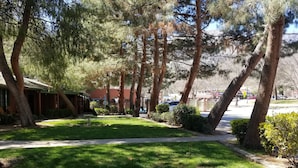 A well-maintained grassy area with trees, a building with a red facade, and a clear sky. - Kernville Inn (Kernville)