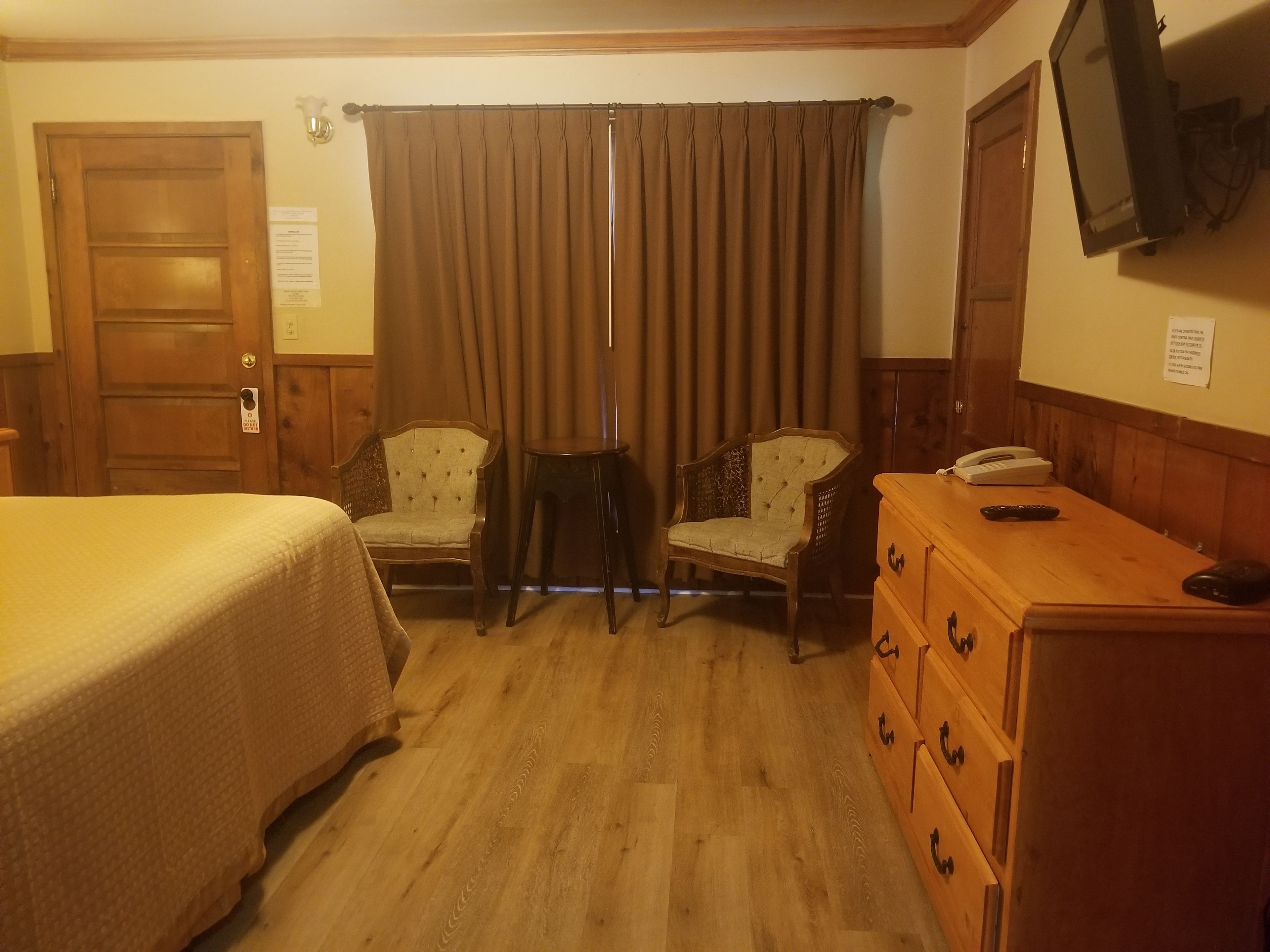 A hotel room with a bed, two chairs, a dresser, a television, and a wooden door.