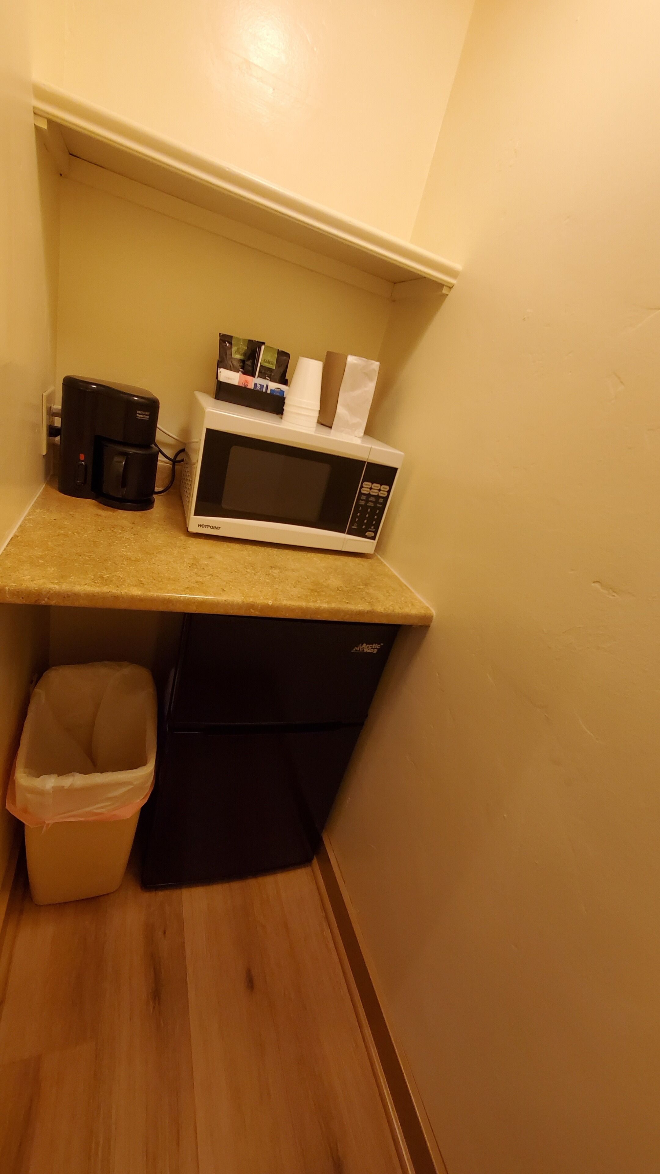 A kitchenette with a microwave, coffee maker, and a trash bin.