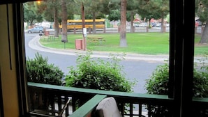 A view from a window with a green railing, overlooking a street with a yellow school bus, cars, and a grassy area with trees. - Kernville Inn (Kernville)