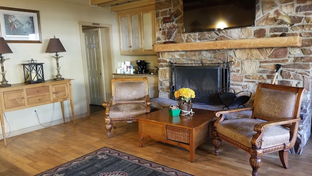 A cozy living room with a stone fireplace, wooden furniture, and a television mounted on the wall. - Kernville Inn (Kernville)