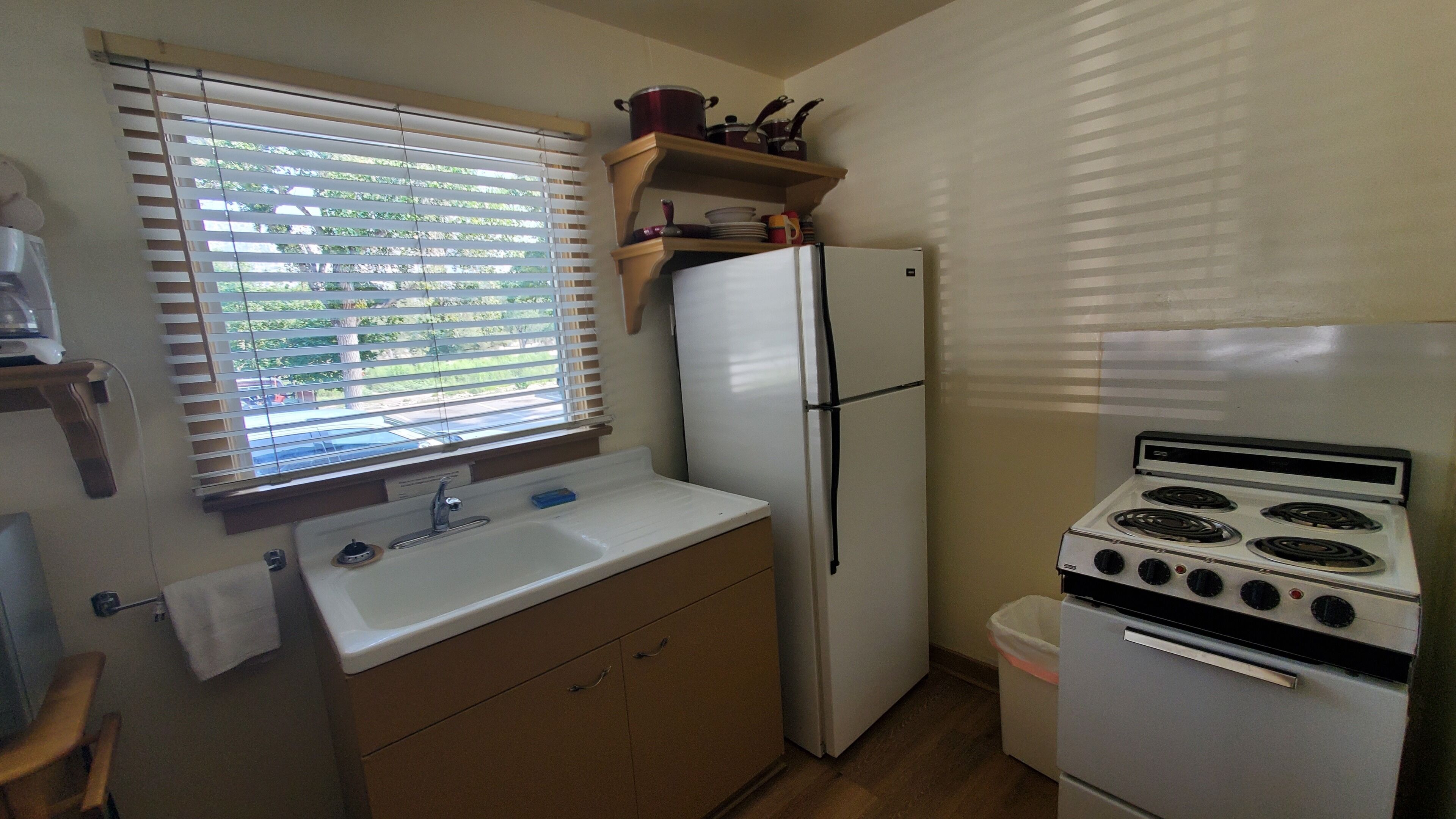 A compact kitchen with a sink, a refrigerator, an oven, and a window with blinds.