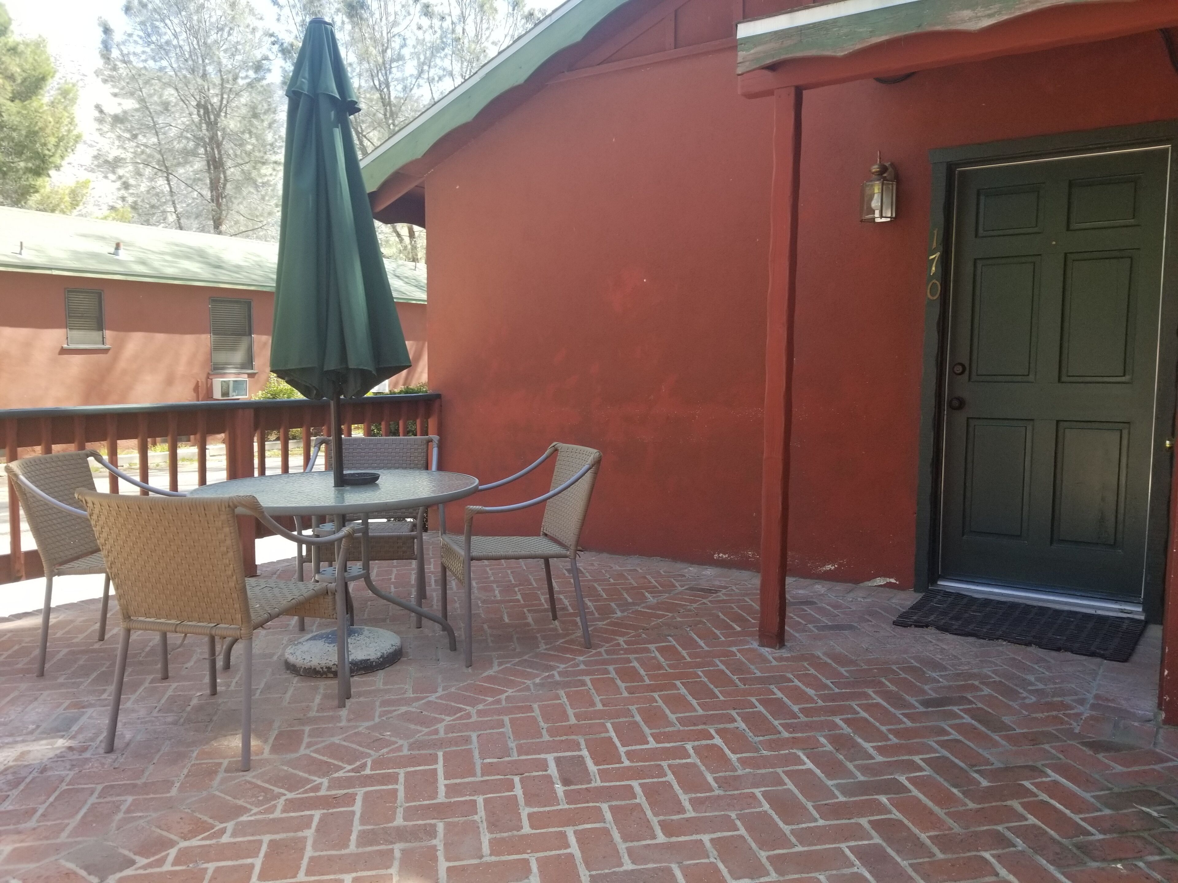 Une terrasse avec un sol en briques, une table entourée de chaises et un parasol vert.