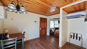 A room with a wooden ceiling, a dining table with chairs, a bed with a mattress and pillows, a TV, and a window with blinds. - Kernville Inn (Kernville)