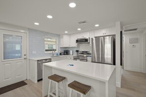 A modern kitchen with white cabinetry, stainless steel appliances, and a central island with stools.