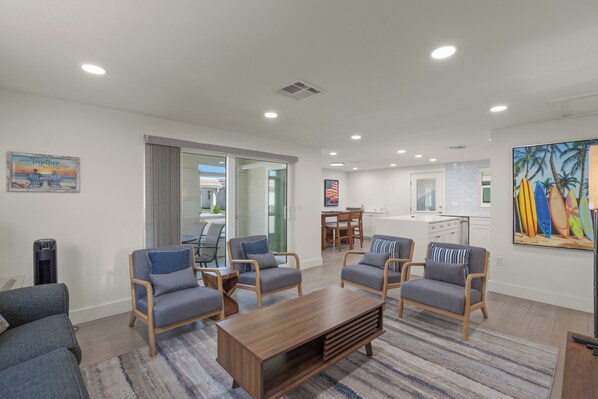 A modern living room with a wooden coffee table, grey sofas, and a dining area with a table and chairs.
