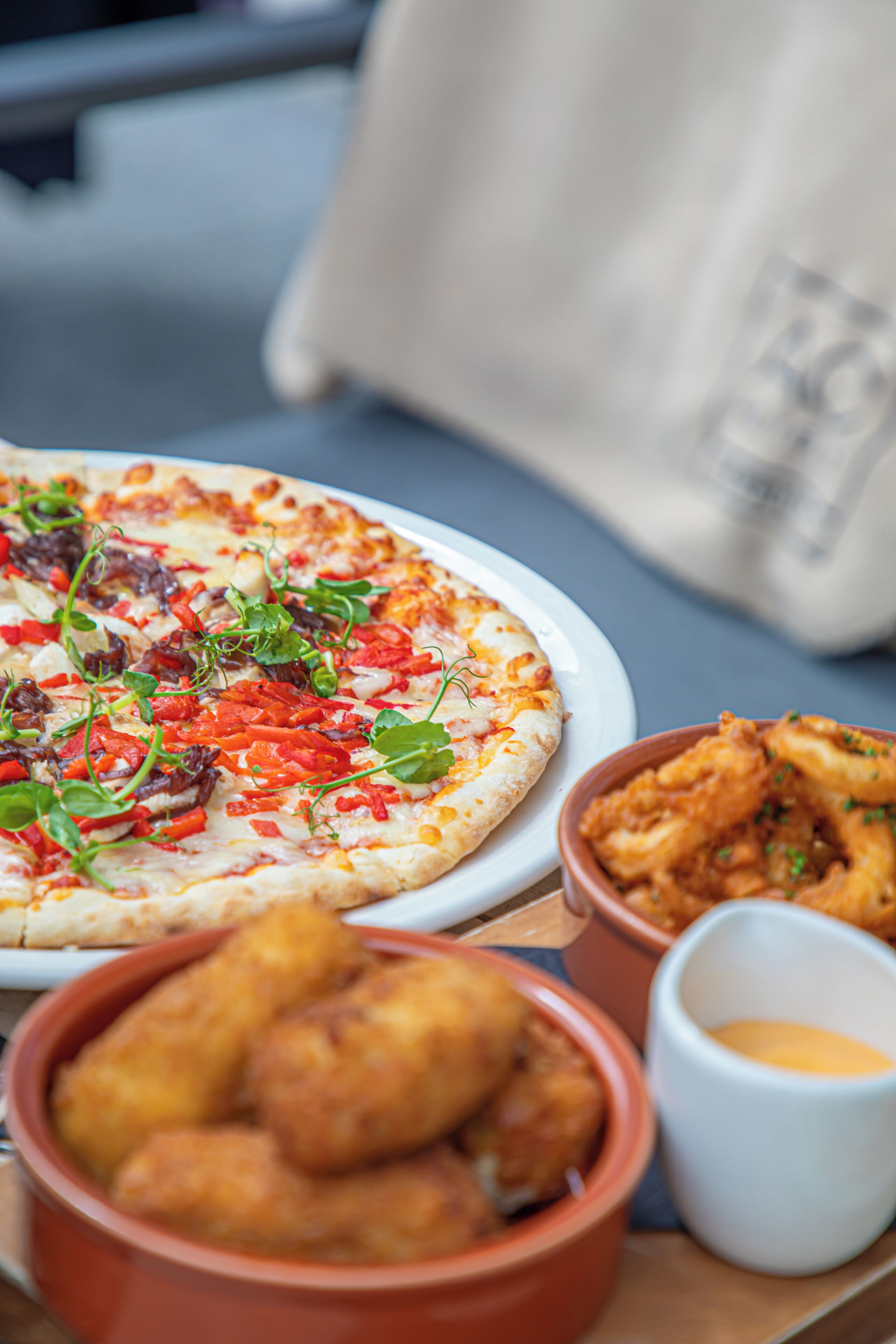 A pizza with toppings and a side of fried food on a table.