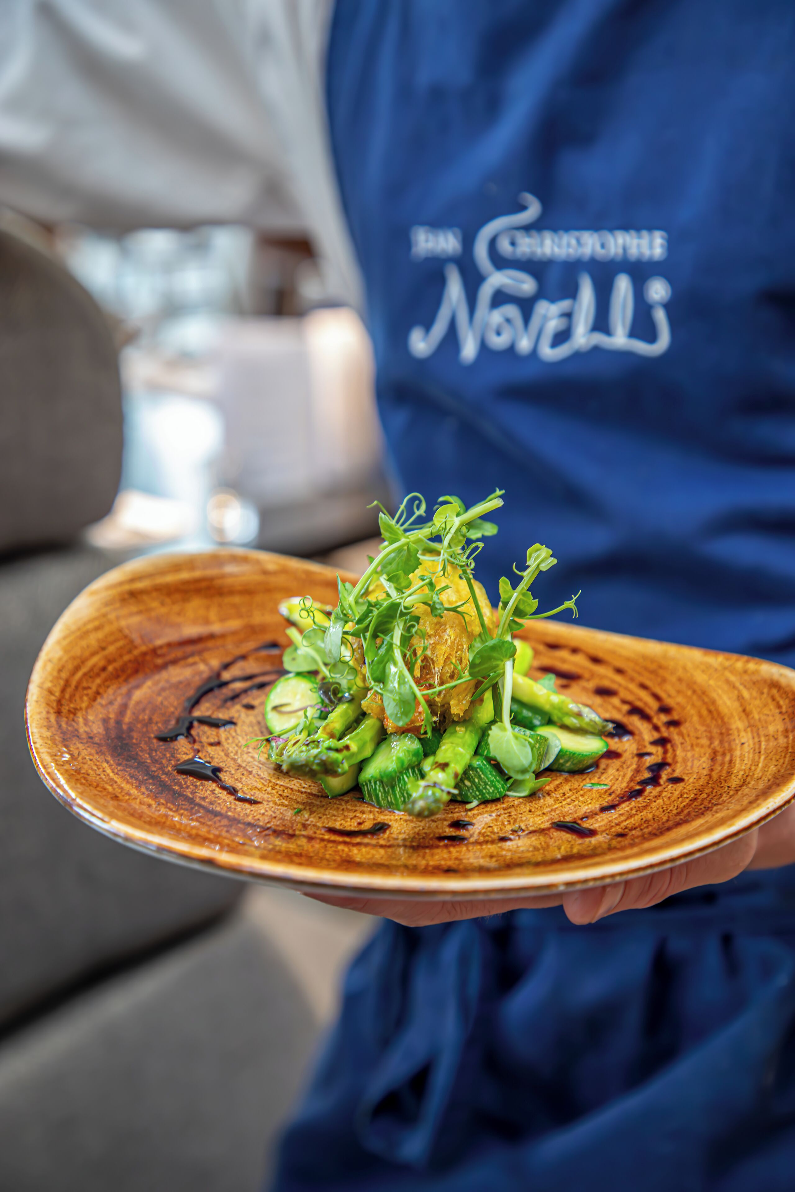 A person holding a plate with a dish of greens and vegetables.