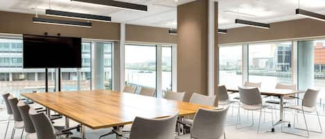 Una sala de conferencias moderna con una gran mesa y sillas, ventanas amplias y un televisor de pantalla plana.