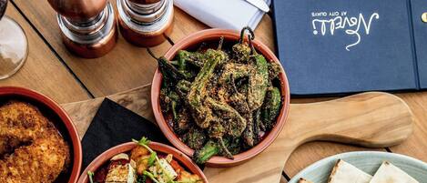 A wooden table with various dishes, including a bowl of roasted vegetables, a plate of flatbreads, and a dish with cubed food and greens.
