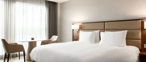 A hotel room with a large bed, a bedside table, a chair, and a window with curtains.