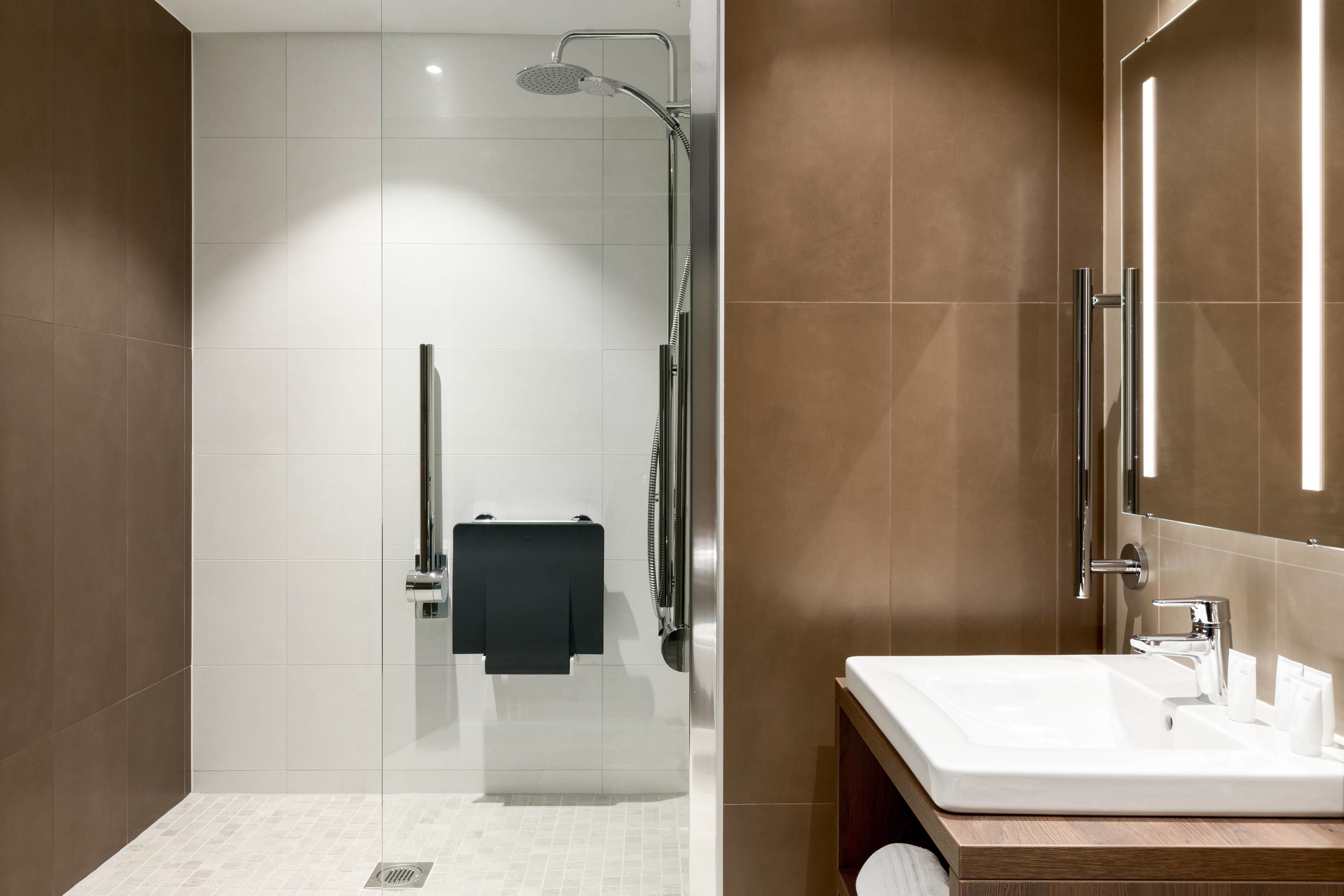 Un baño moderno con ducha envuelta en vidrio, un lavamanos blanco y un mueble de tocador de madera.