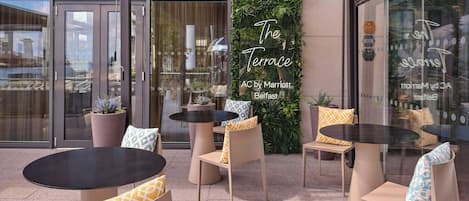 An outdoor seating area with tables and chairs, a green vertical garden, and a neon sign reading "The Terrace AC by Marriott Belfast".