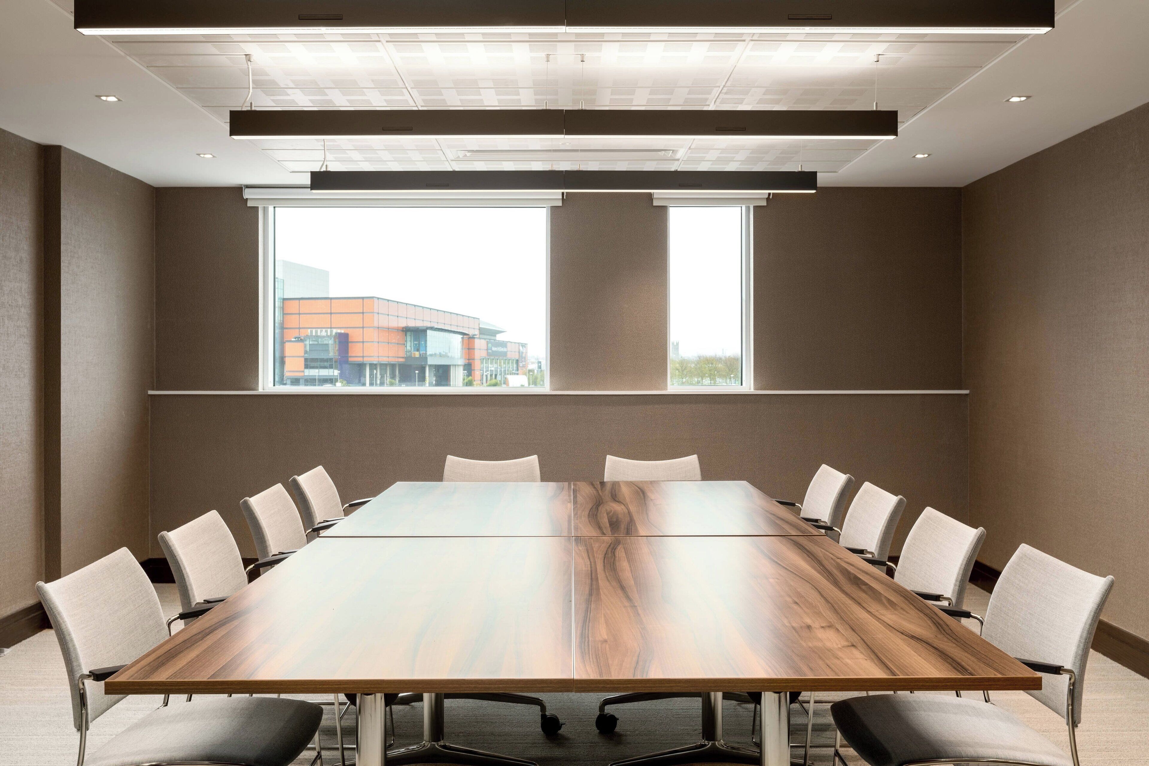 Un salón de conferencias con una larga mesa, sillas y ventanas amplias.